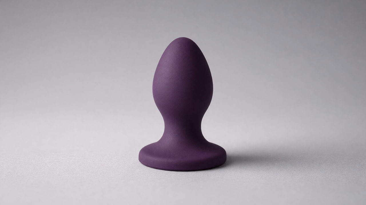 Een grote siliconen buttplug met brede uitlopende voet op een lichte ondergrond