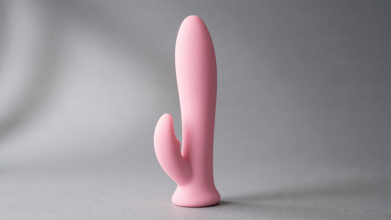 Een roze duotype vibrator met een schacht en een kleinere buitenarm, los staand op een neutrale ondergrond