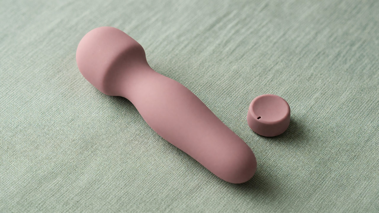 Een siliconen vibrator in zachtroze op een licht linnen oppervlak, naast een draaiknop op een lage stand