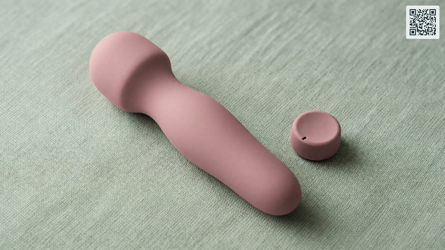 Een siliconen vibrator in zachtroze op een licht linnen oppervlak, naast een draaiknop op een lage stand