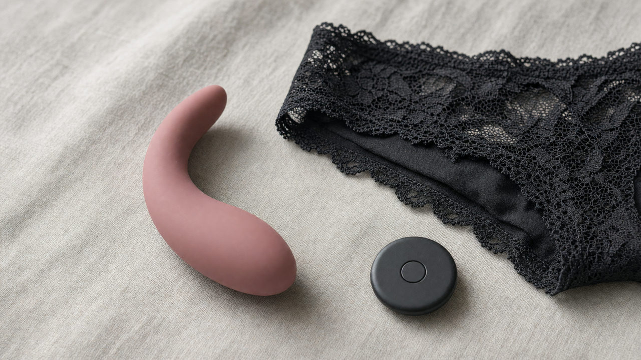 Een gebogen siliconen wearable vibrator naast donker ondergoed en een kleine ronde afstandsbediening op een linnen ondergrond